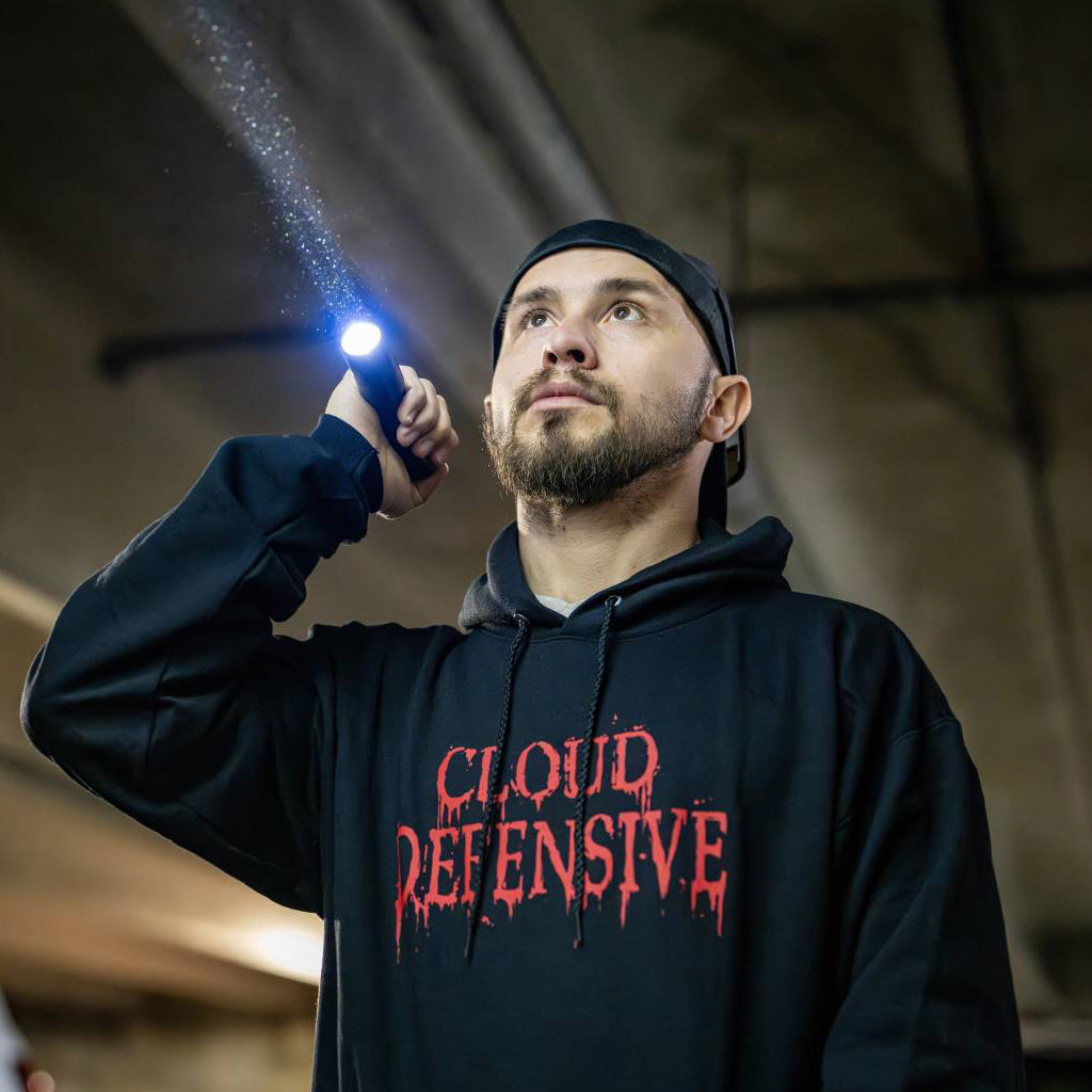 Man in a black hoodie holding a flashlight.