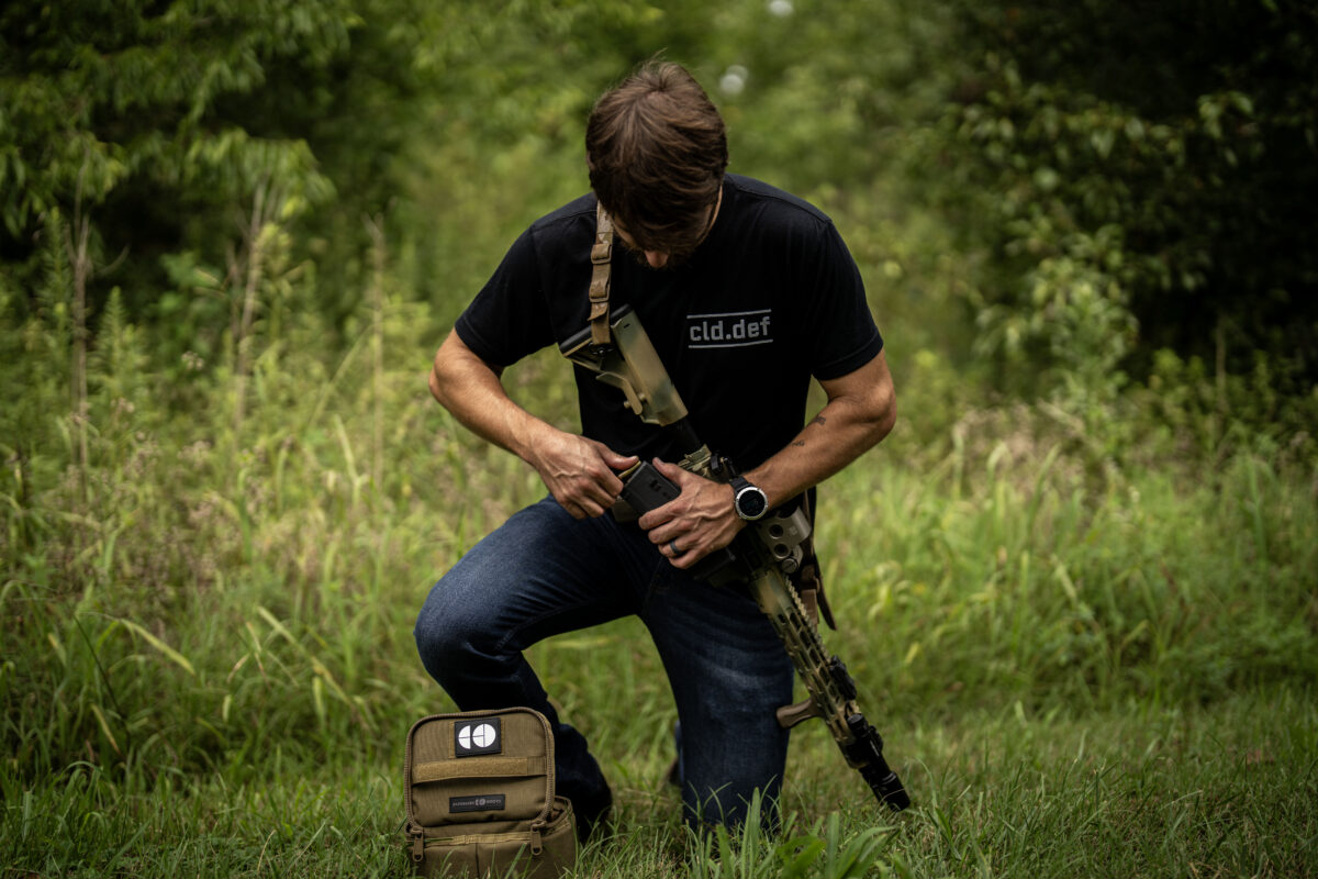 Man kneeling on grass and loading magazine.