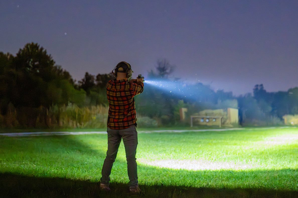 Man standing in field pointing a pistol with a flashlight.