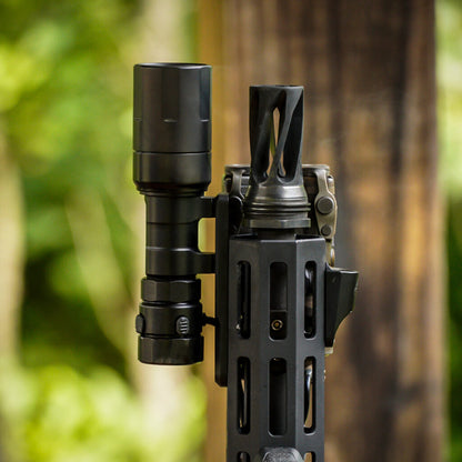 close up of black Rein Micro flashlight mounted to a rifle and next to muzzle device. Bottom view.