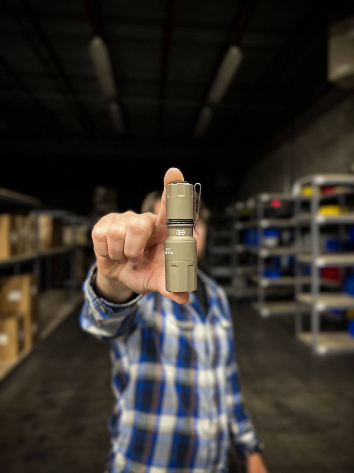 Man holding FDE MCH Micro flashlight in his fingers towards camera.